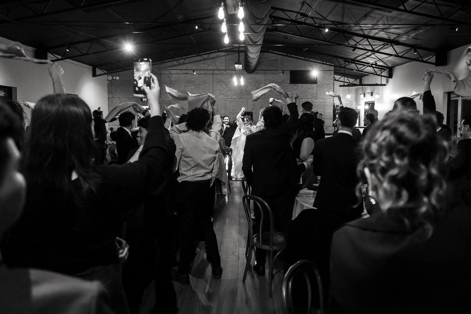 Black and white wedding reception photo showing guests dancing and celebrating in an elegant venue.