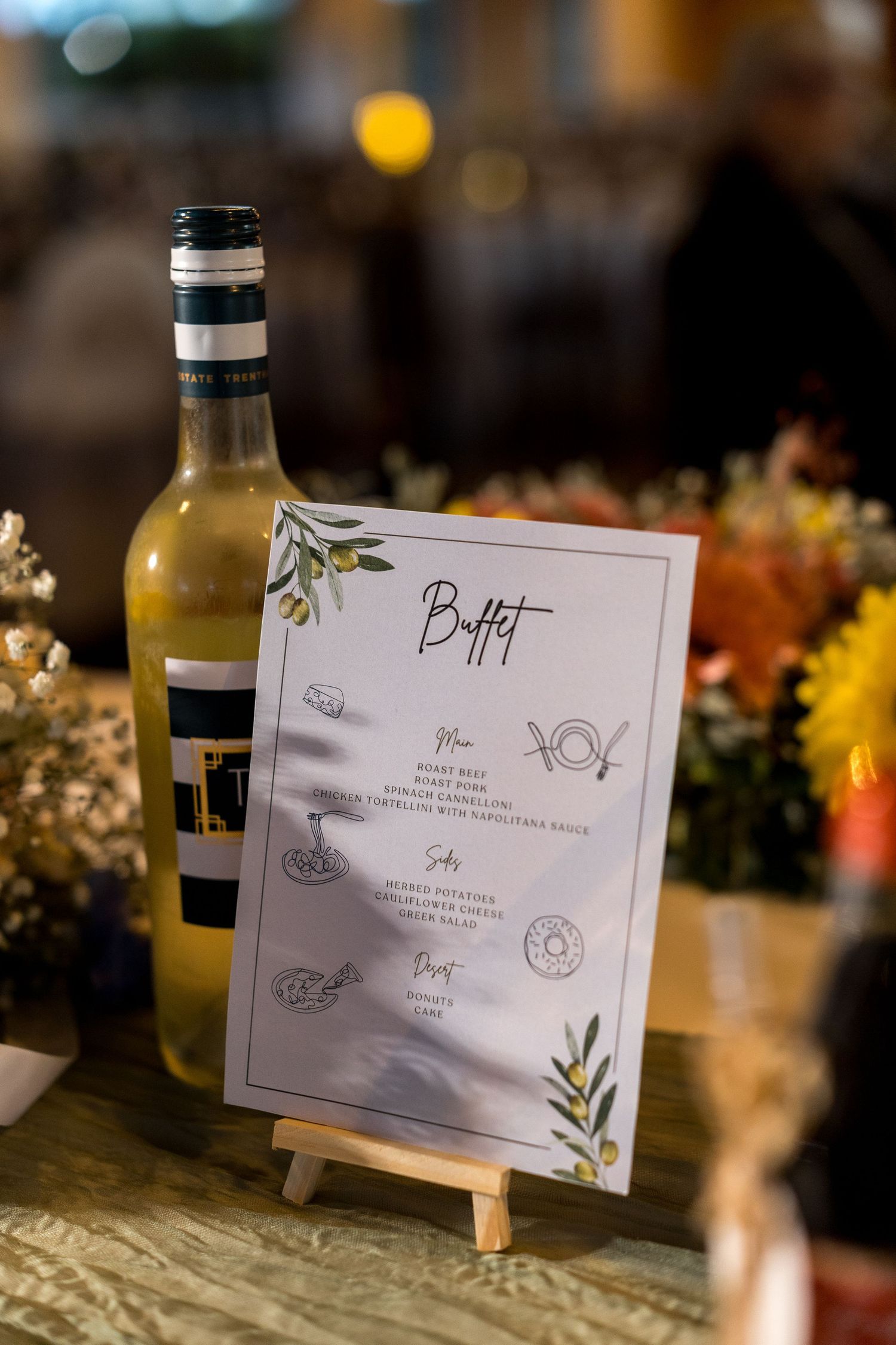 Elegant buffet menu card on easel next to white wine bottle at wedding reception.