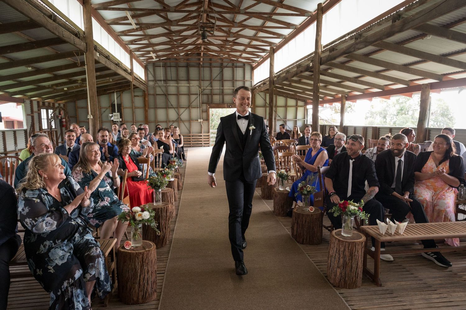 Wedding guests seated in rustic barn venue during ceremony proceedings.