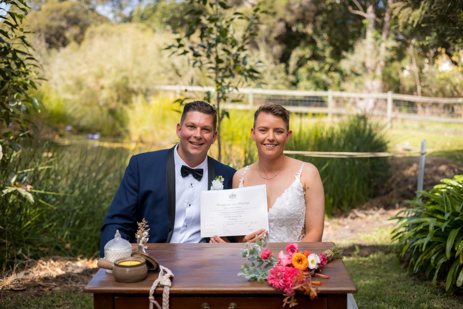 Wedding party enjoys outdoor reception at decorated tables in garden setting.