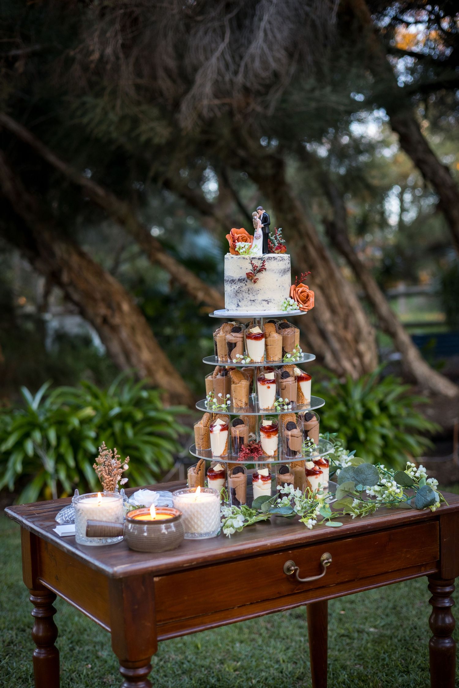 Elegant tiered wedding cake display on a vintage wooden table in a garden setting at dusk.