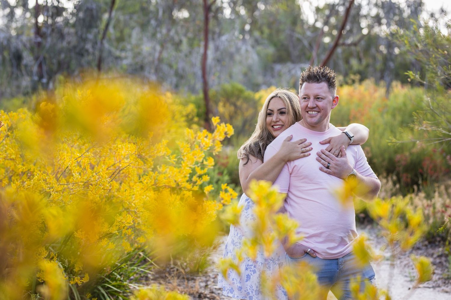 at Kings Park, Couple embracing and smiling among vibrant yellow wildflowers in a lush outdoor setting.