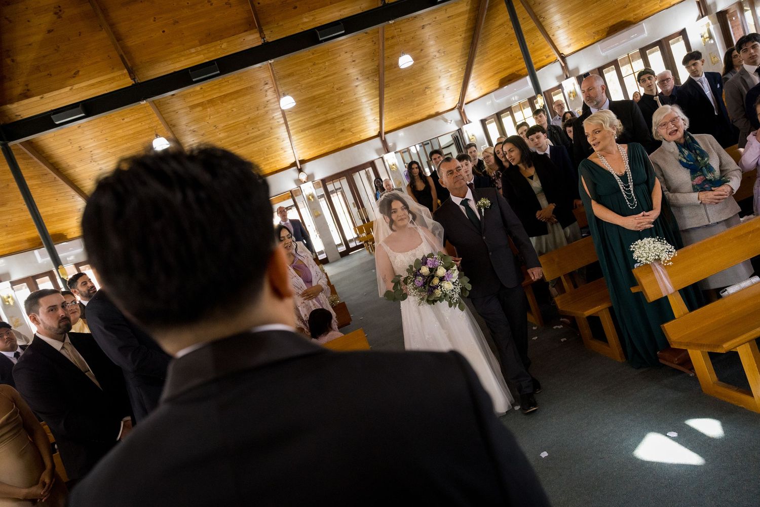 Wedding ceremony in progress inside wooden chapel with natural lighting.