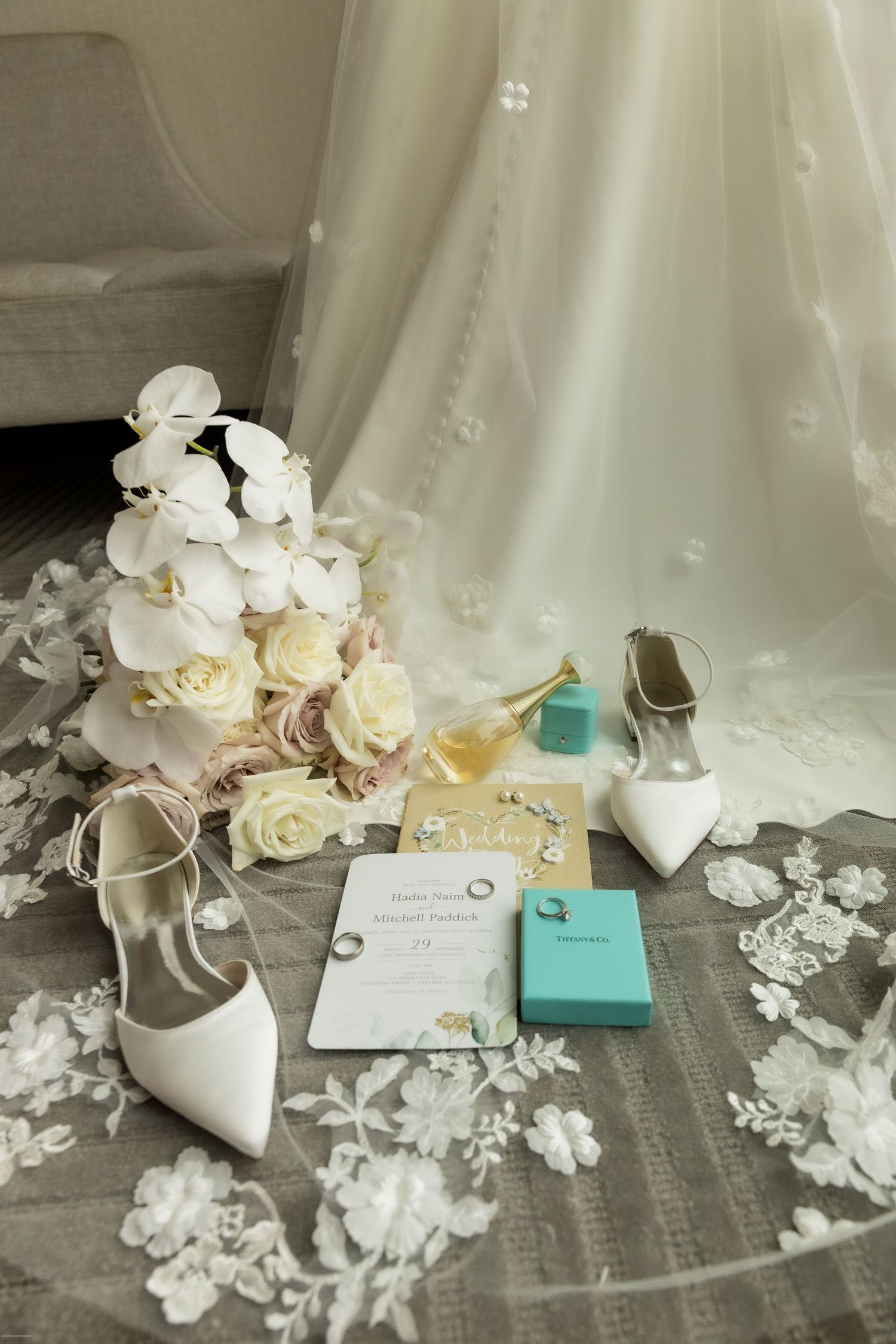 Wedding flat lay with bridal bouquet, white heels, Tiffany boxes, and invitation.