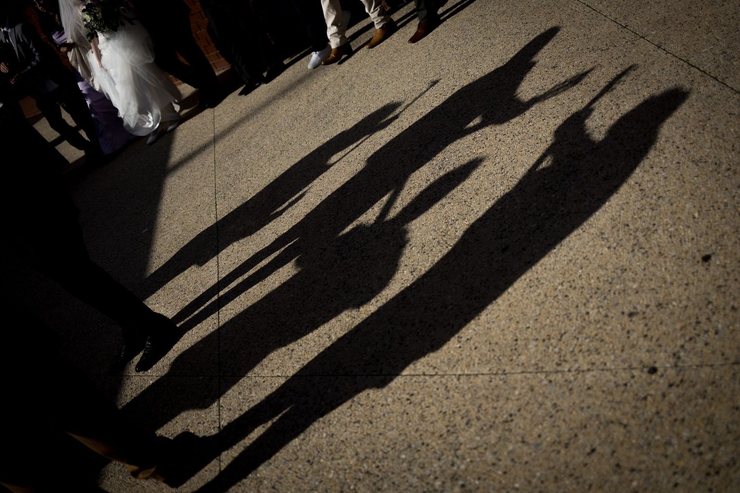 Long shadows of wedding guests cast on concrete ground at sunset.