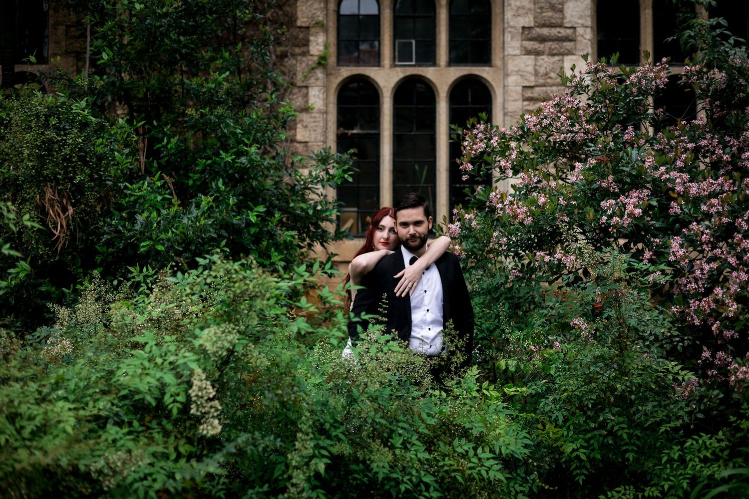Gothic stone building with arched windows surrounded by lush garden foliage.