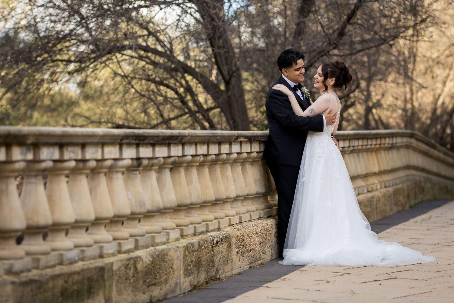 A bride and groom share a romantic moment on a stone bridge surrounded by autumn trees in an outdoor wedding photo at Caversham House