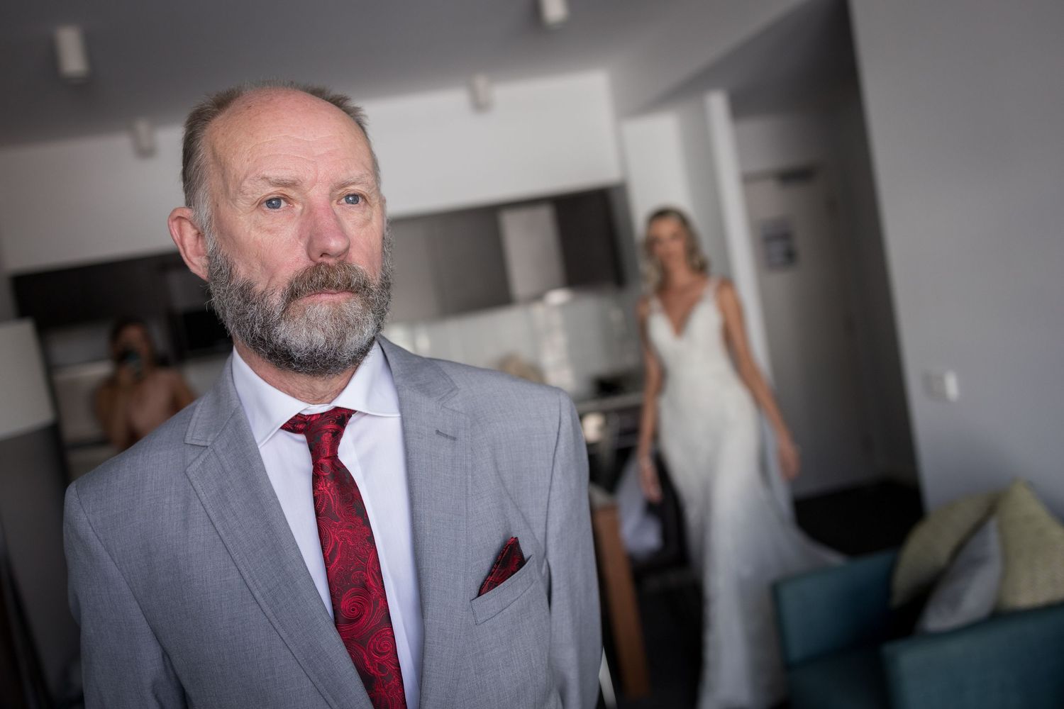 Groom in grey suit and red tie prepares for wedding ceremony.