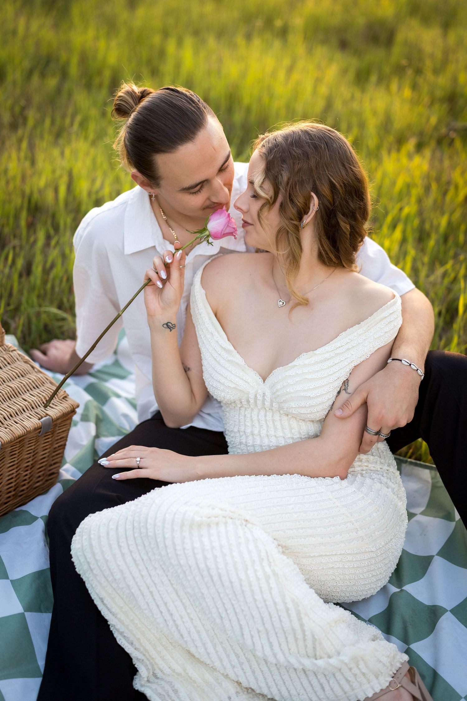 Couple sharing a romantic picnic on a green checkered blanket in a meadow, woman in white dress holding a pink rose. at Guildford, Perth
