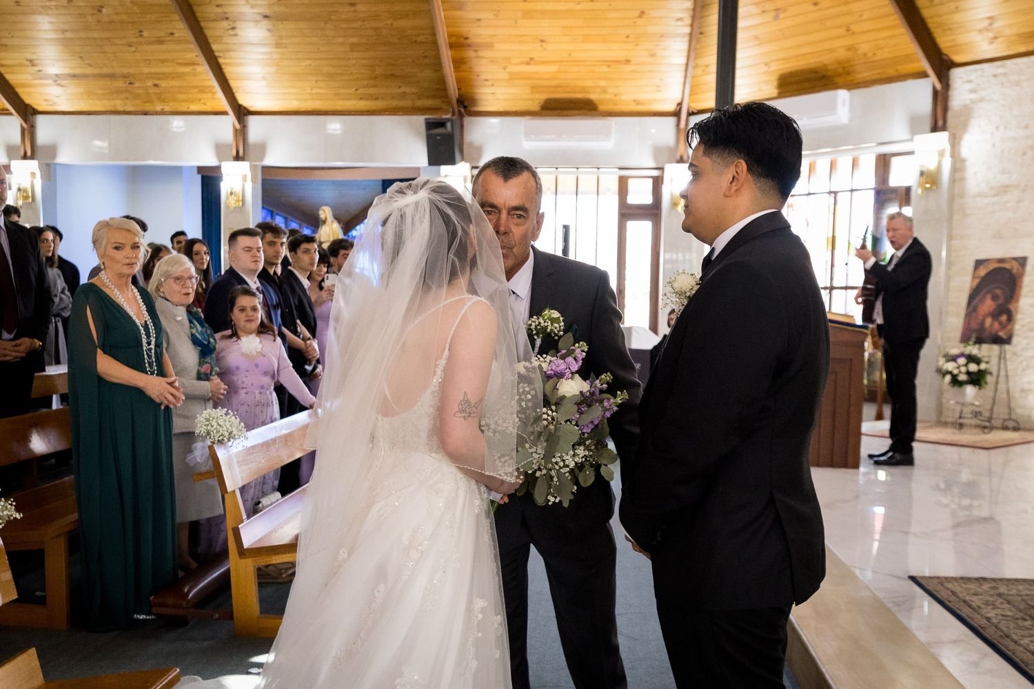 Wedding ceremony taking place in bright church interior with wooden beams.