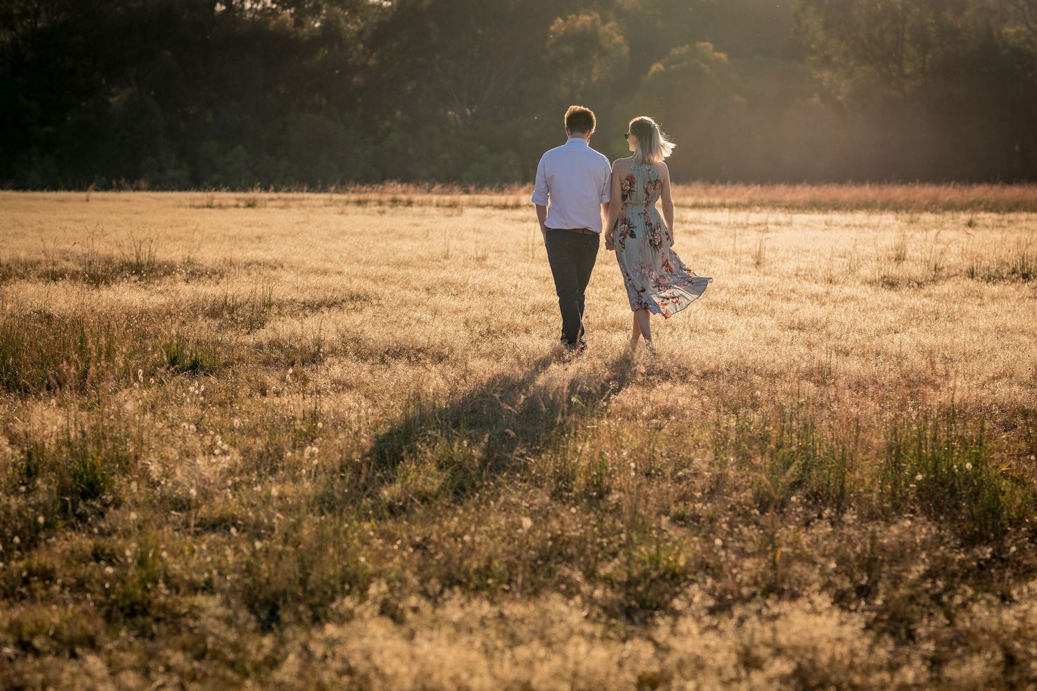 Silhouettes of a couple walking through a sun-drenched field at golden hour.