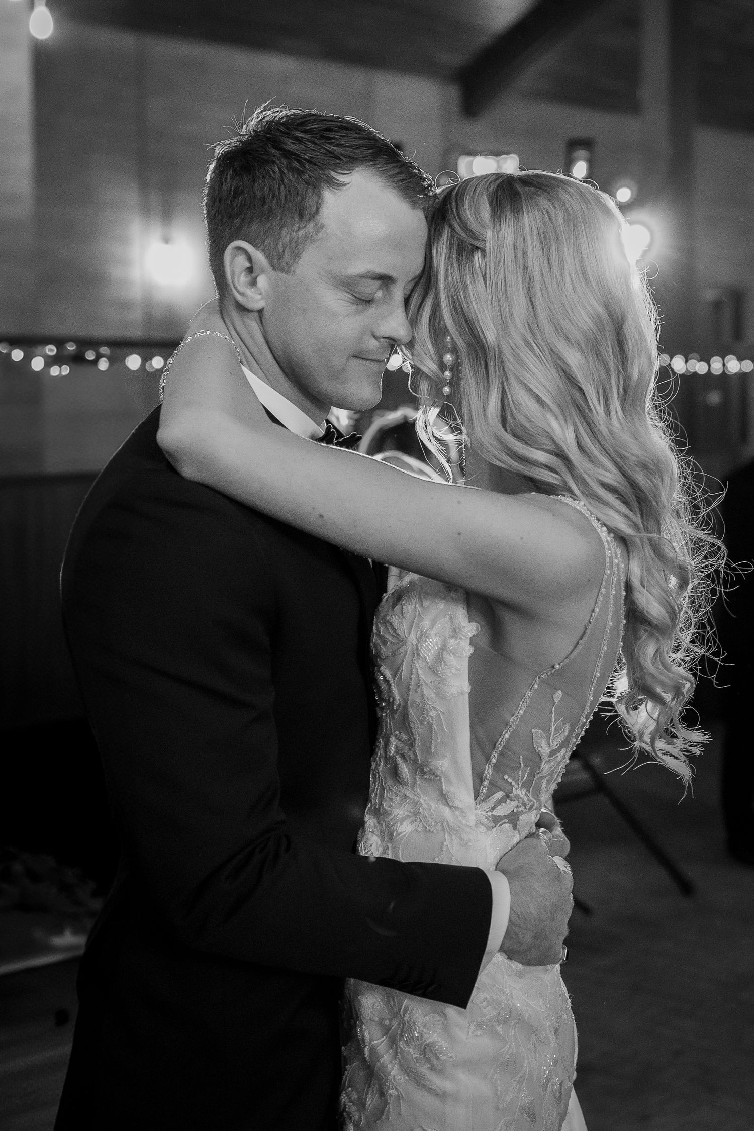 Bride and groom sharing an intimate first dance in black and white with bokeh lights.