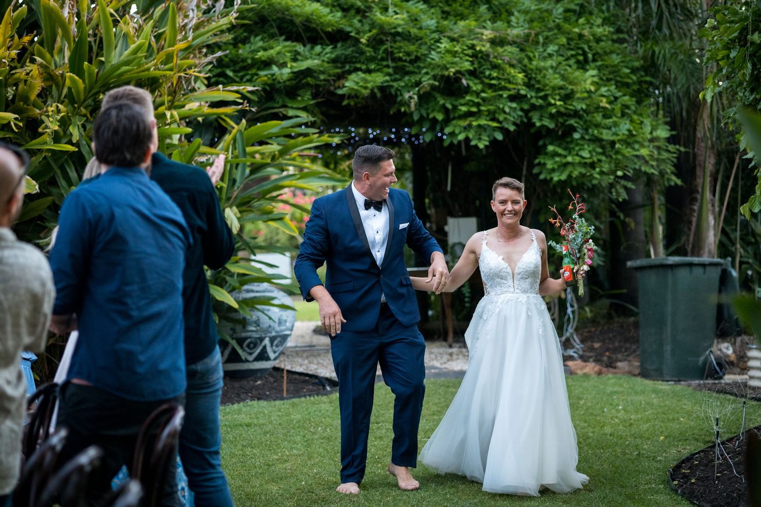 Wedding guests gathered in an outdoor garden ceremony space surrounded by lush greenery.