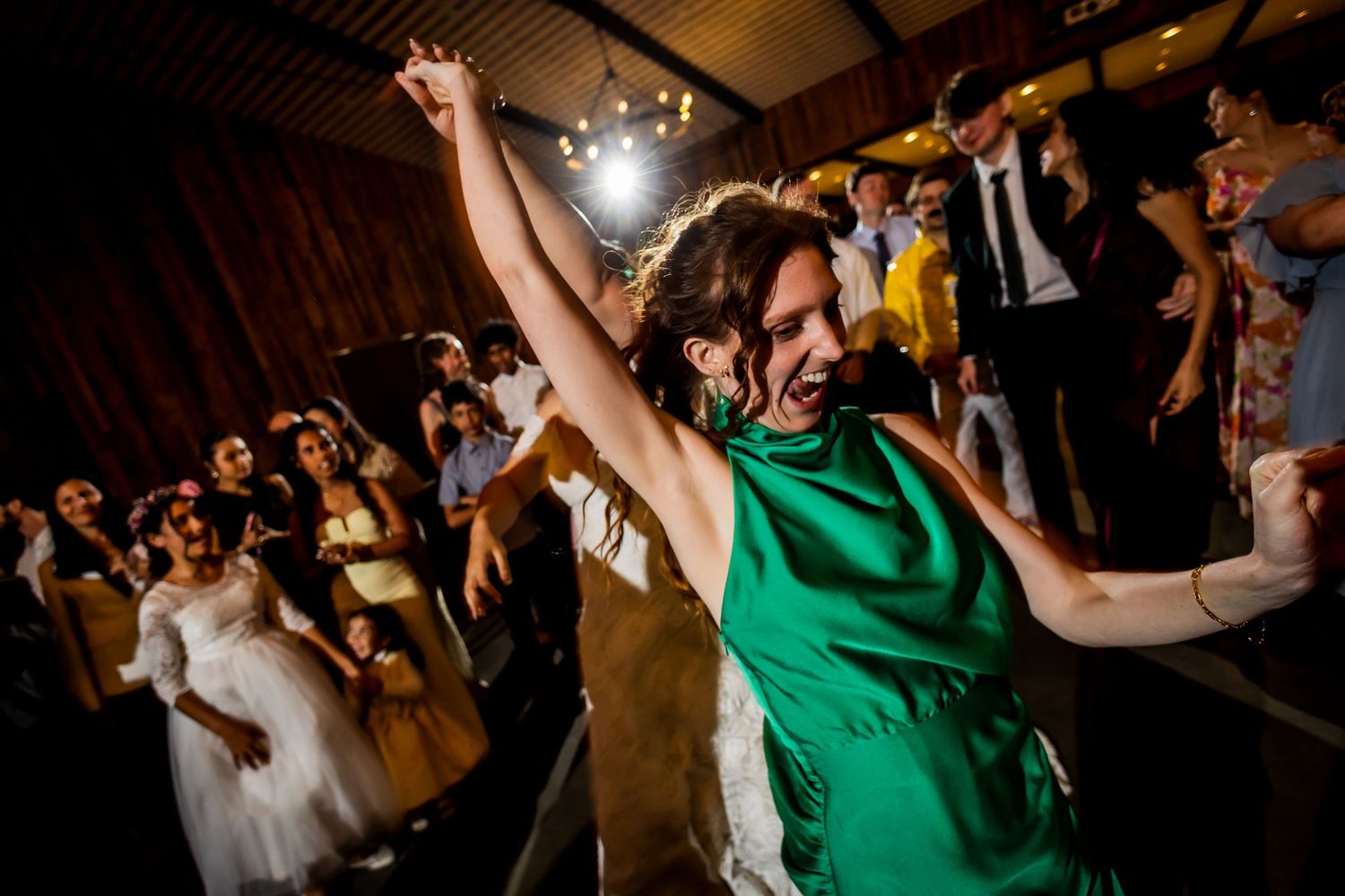 Woman in green dress dancing joyfully at a wedding reception with guests celebrating in the background.