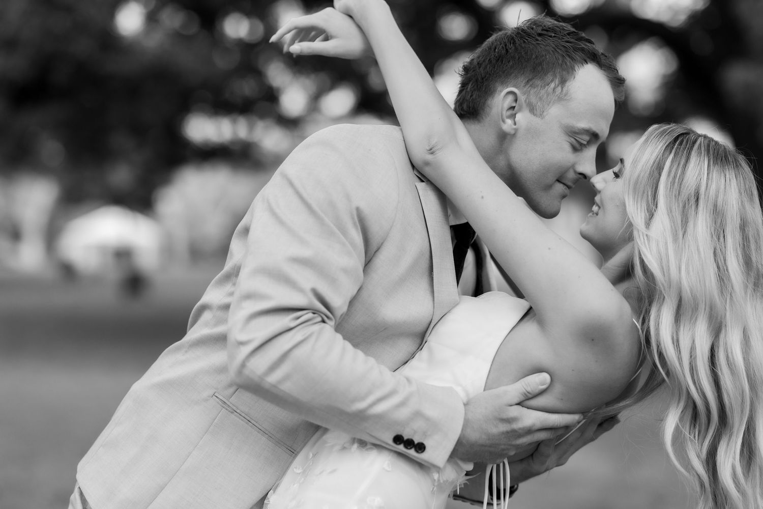 Black and white photo of a couple sharing a romantic dip and almost-kiss at their outdoor wedding celebration.