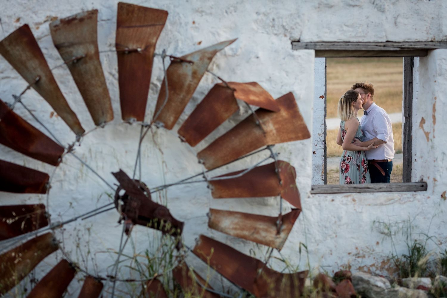 A rustic windmill wheel against white wall with person in window frame.