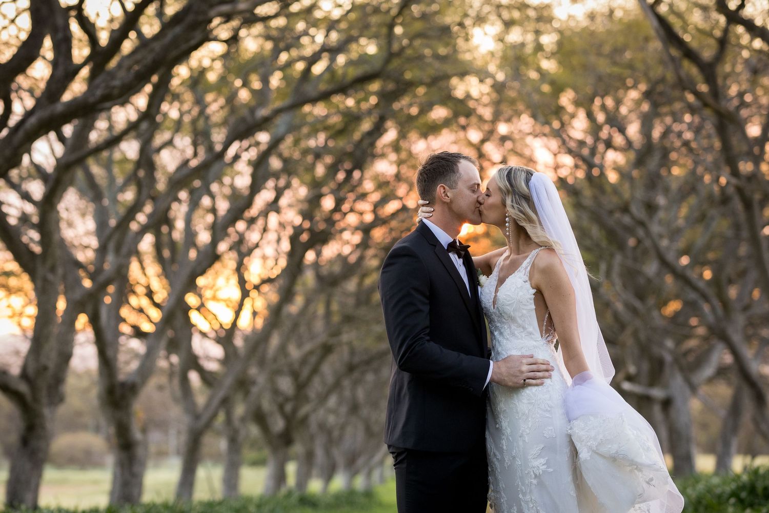 Newlyweds share intimate moments in a rustic orchard at sunset.