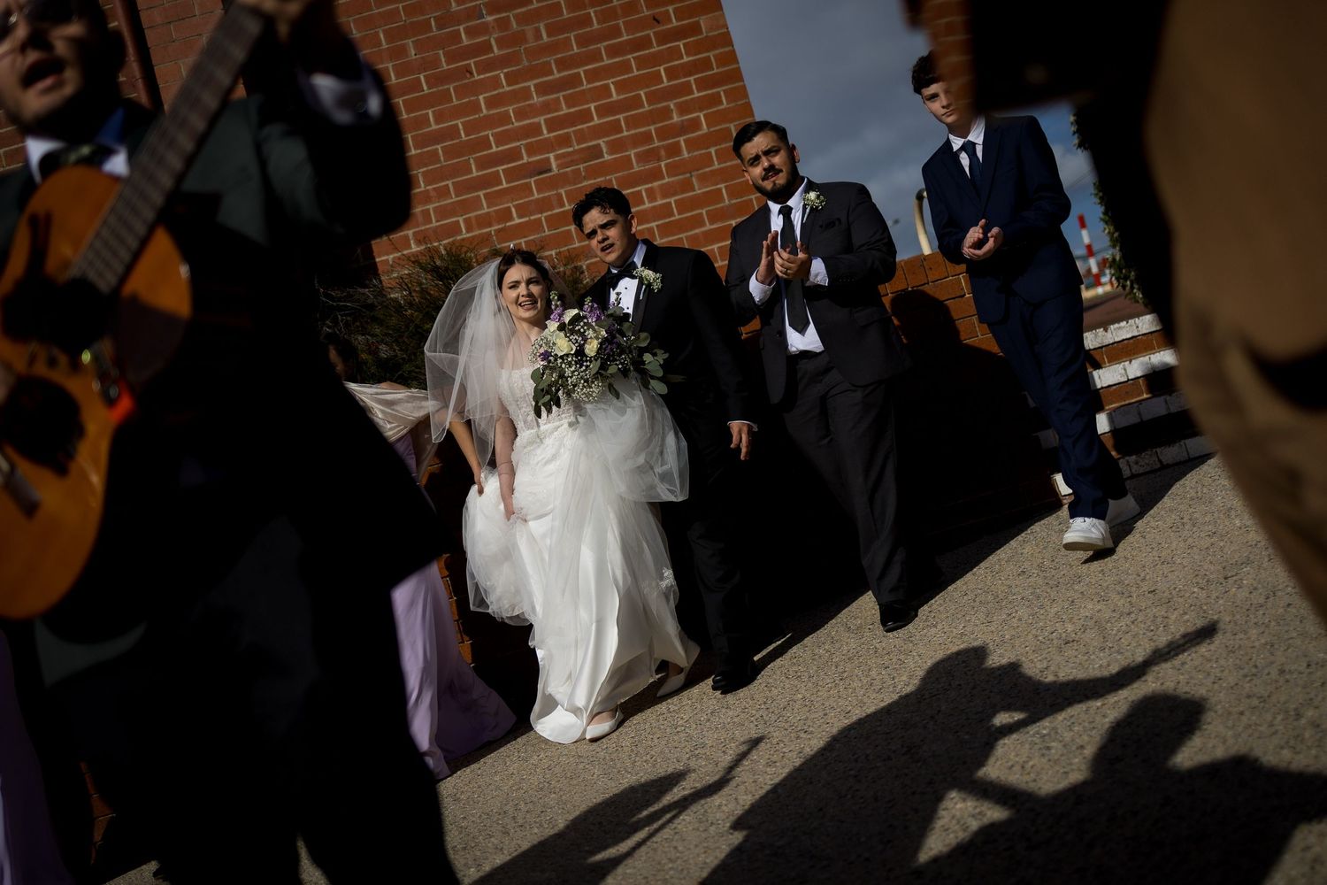 Wedding party gathered outside a brick building casting long shadows.