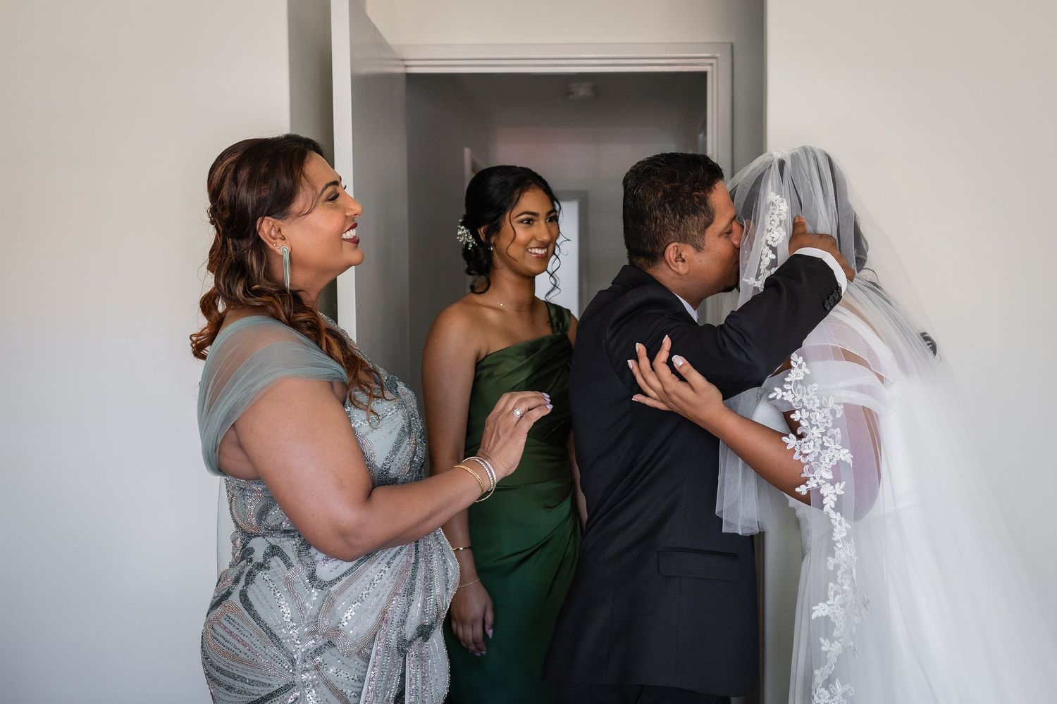 Groom sharing an emotional moment with bride as bridesmaids and family look on during wedding preparations.