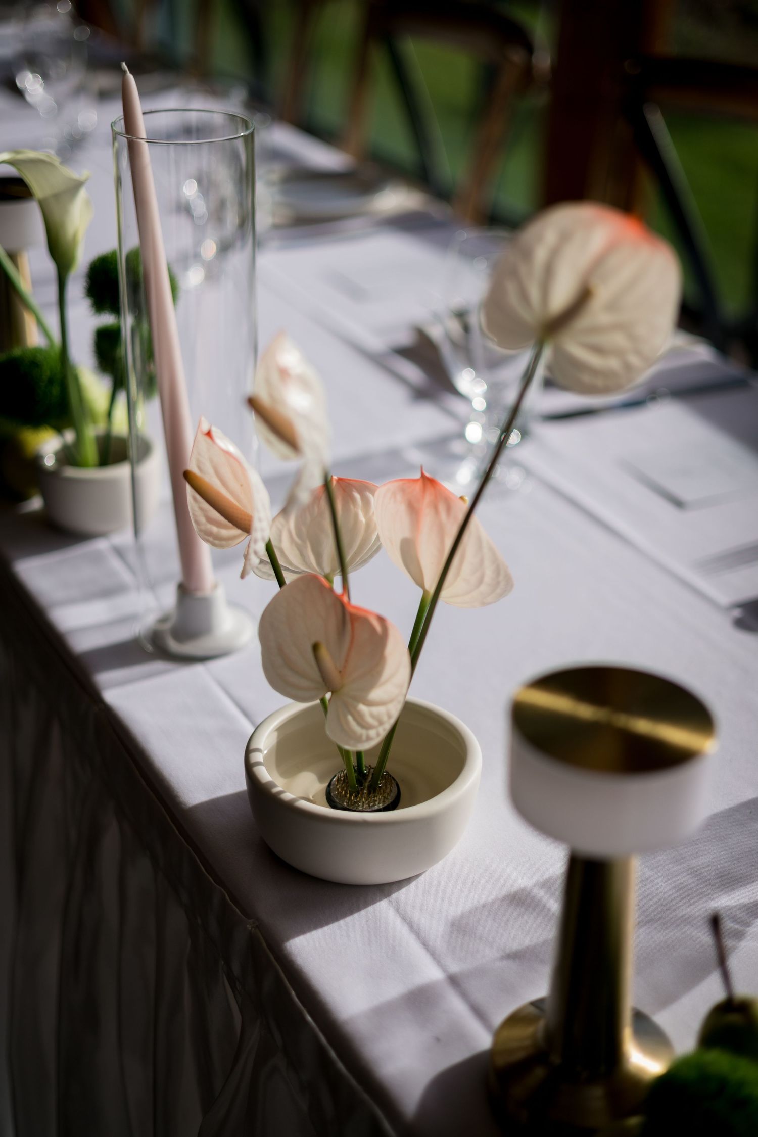 Elegant white anthurium flowers in modern vases decorate a formal table setting.