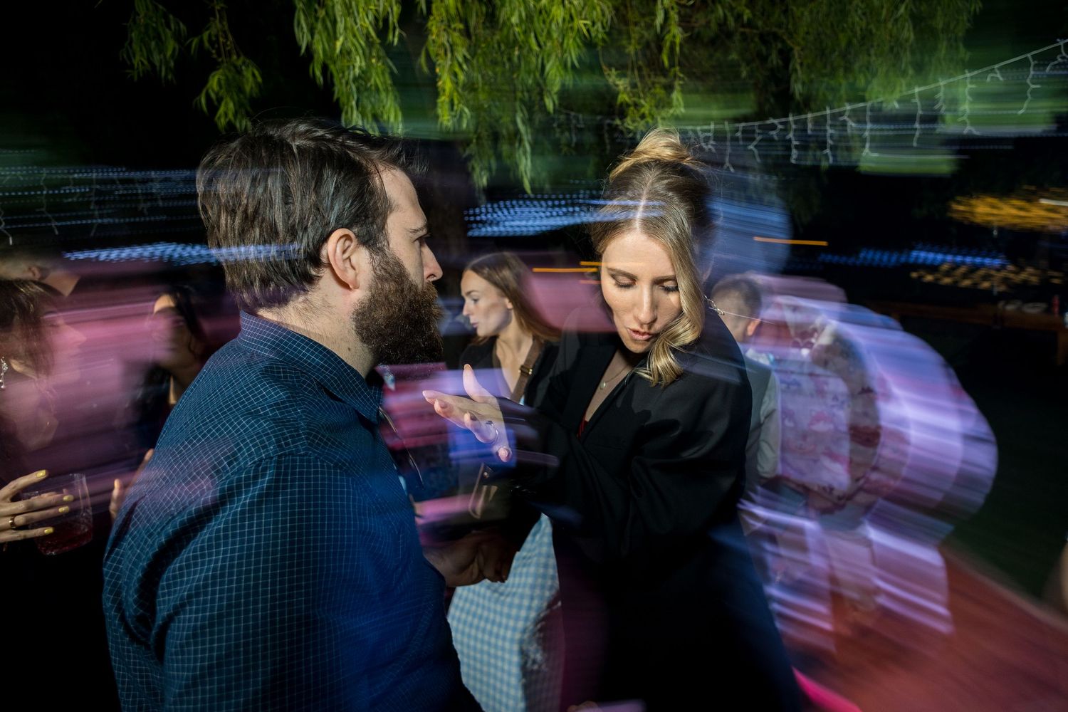 Wedding guests dance and celebrate on an outdoor dance floor illuminated by string lights.
