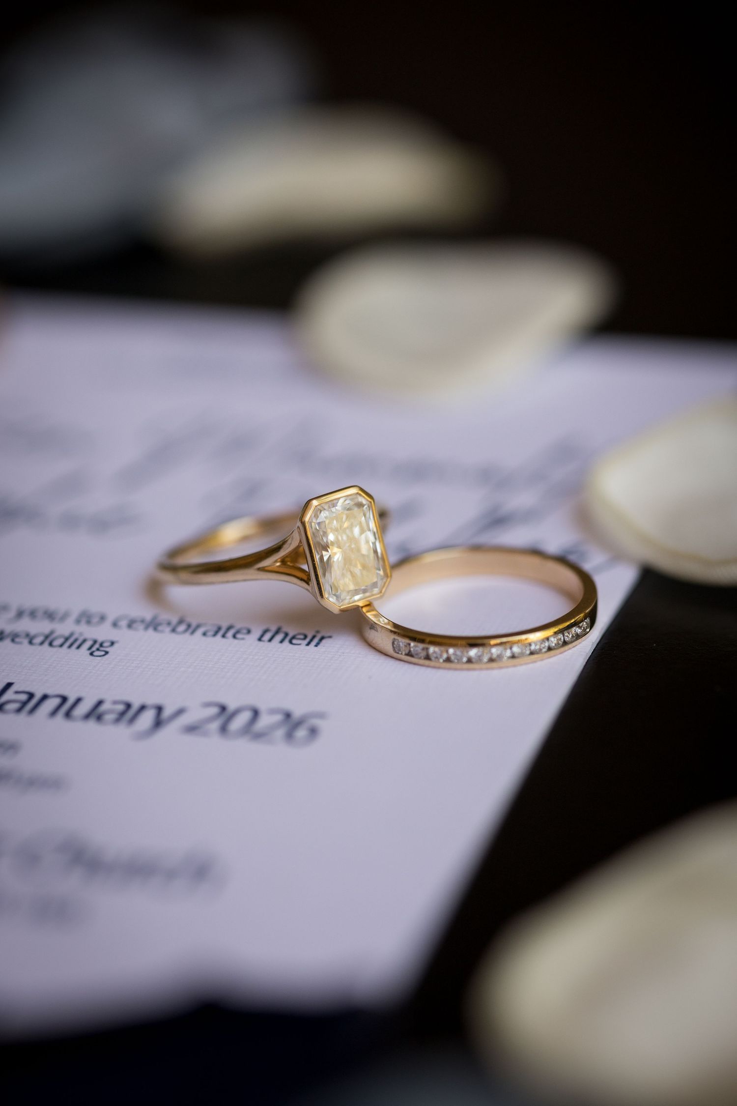 Elegant gold engagement ring with emerald-cut diamond and diamond band on wedding invitation.