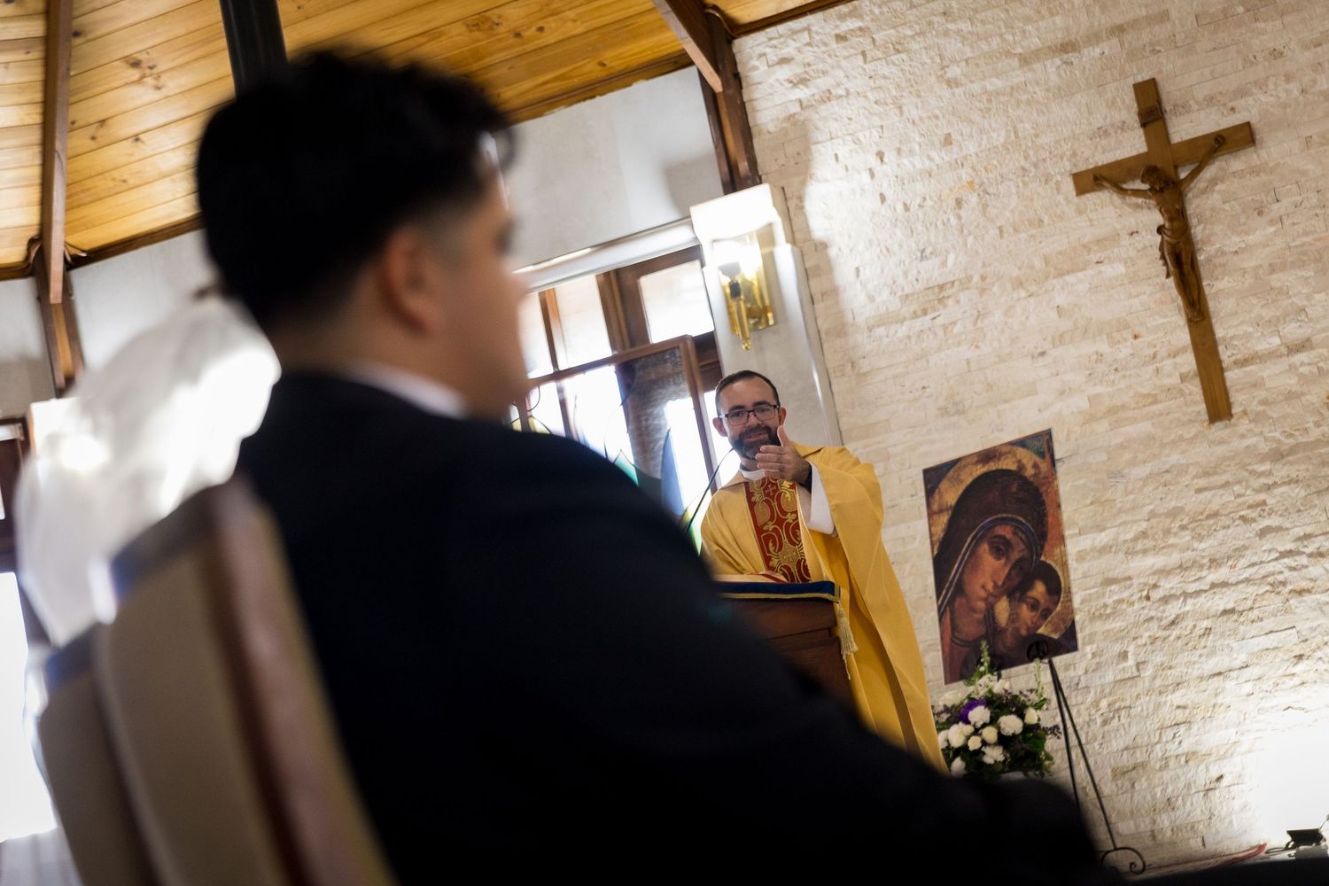 A church wedding ceremony takes place in a beautiful stone chapel with wooden beams and religious artwork.