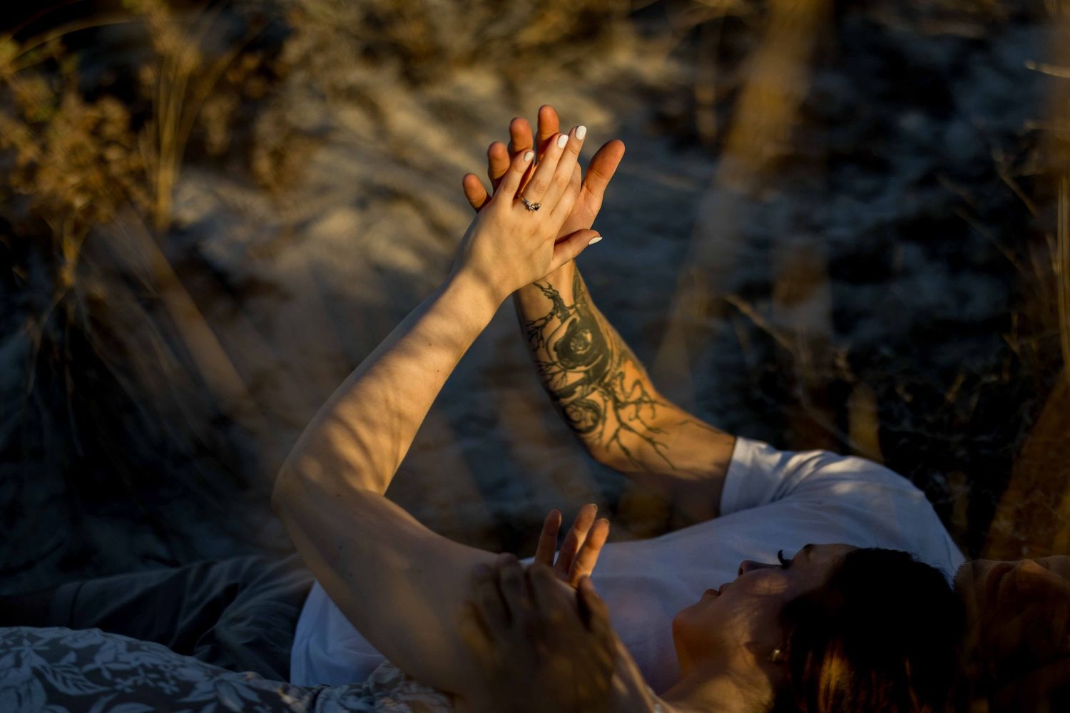Close-up of tattooed couple holding hands raised against warm sunset light outdoors.