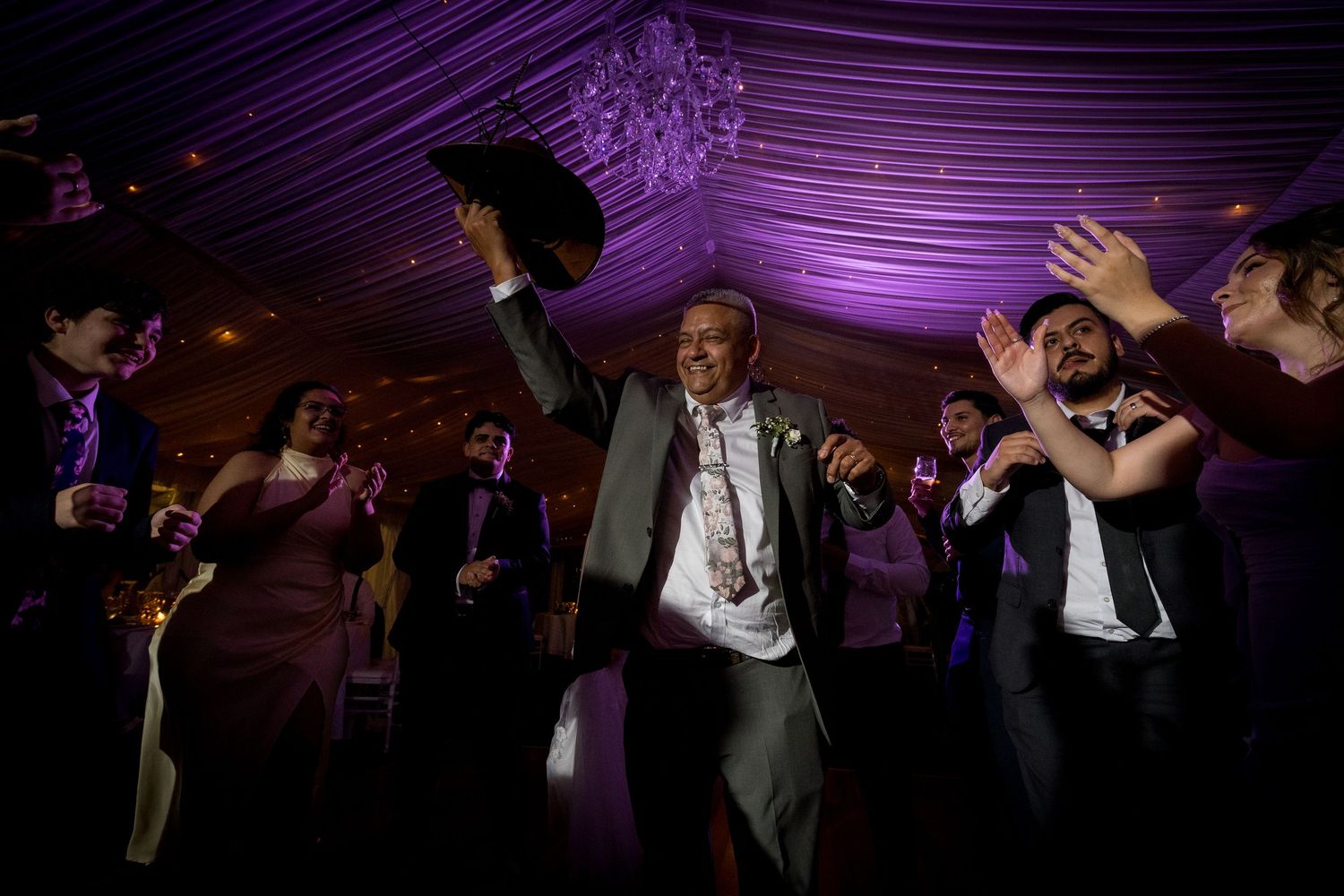 Wedding guests dancing energetically under purple mood lighting at reception.