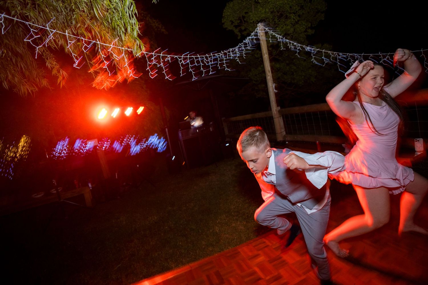 Group dancing energetically at a nighttime outdoor wedding reception with colorful lighting.