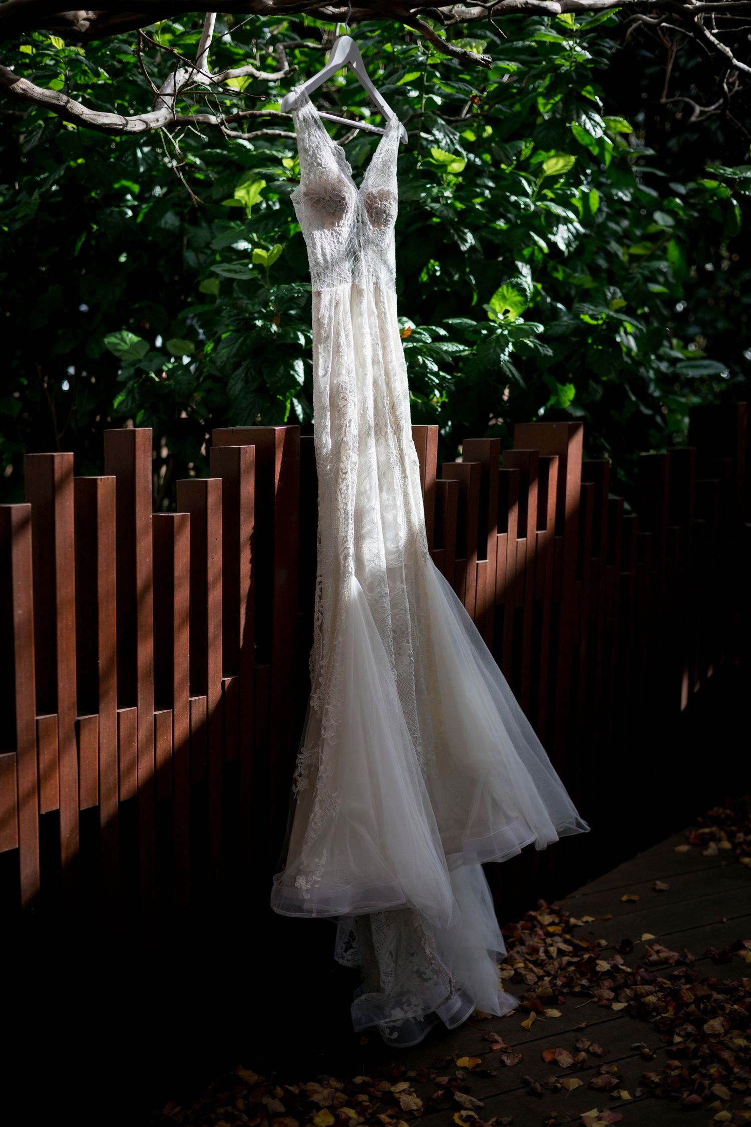 White wedding dresses displayed on hangers against a natural green backdrop.