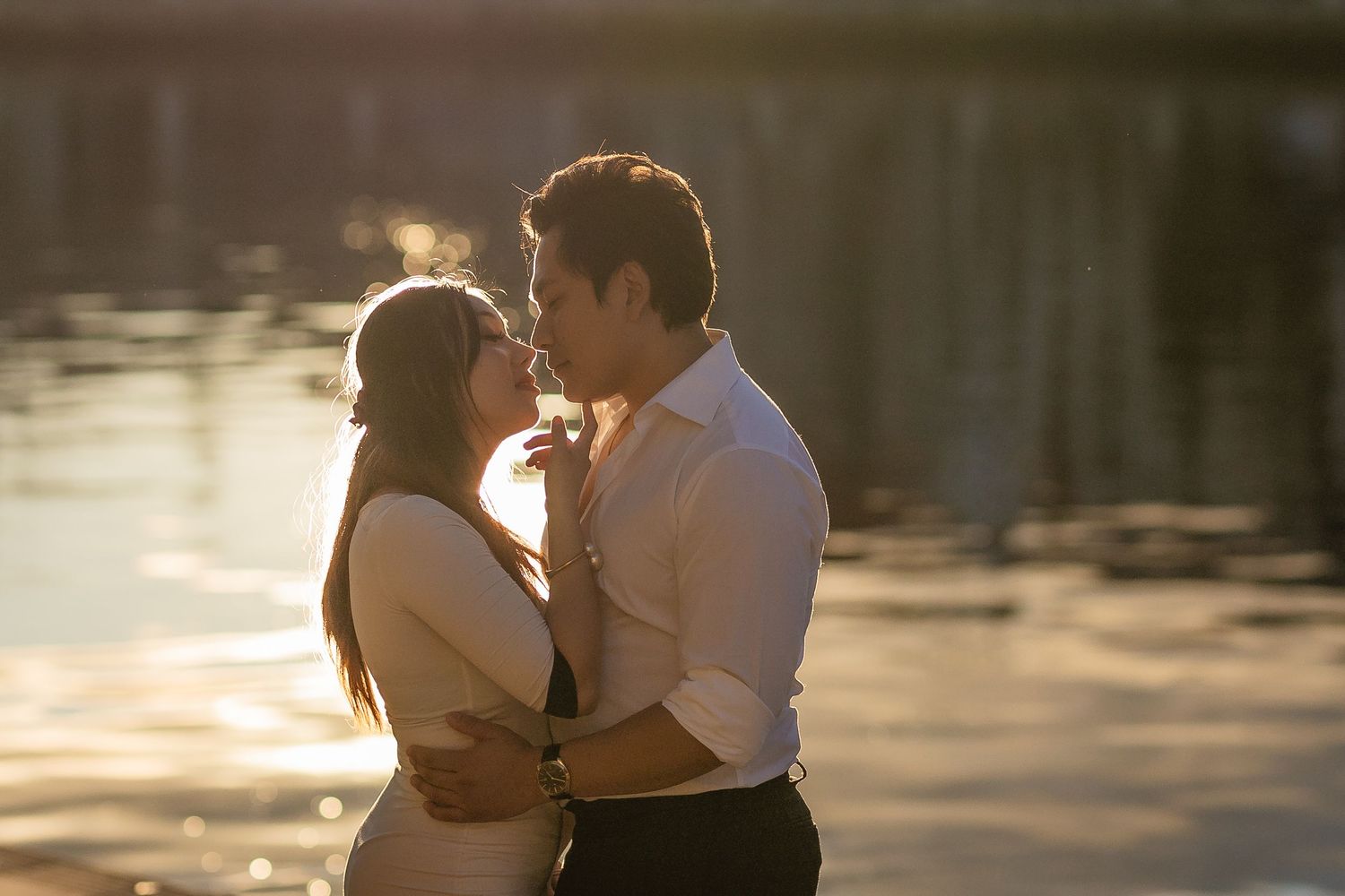 Romantic couple almost kissing by shimmering lake at golden hour sunset.