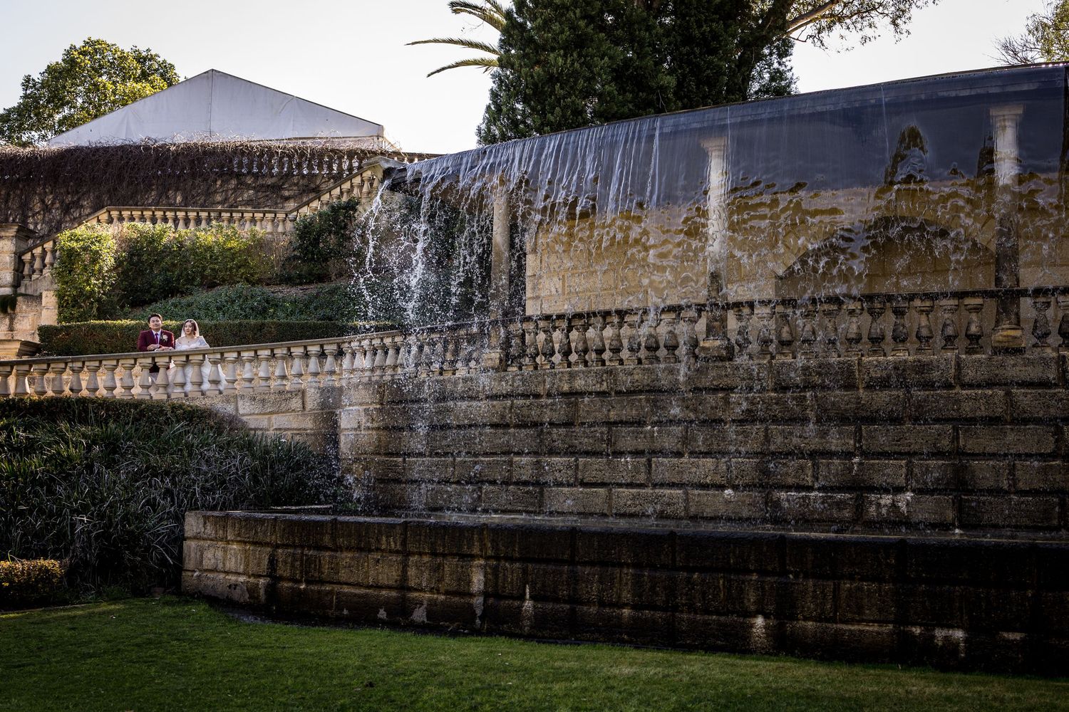 A cascading stone waterfall wall in a lush garden park with ornate balustrade details at dusk.