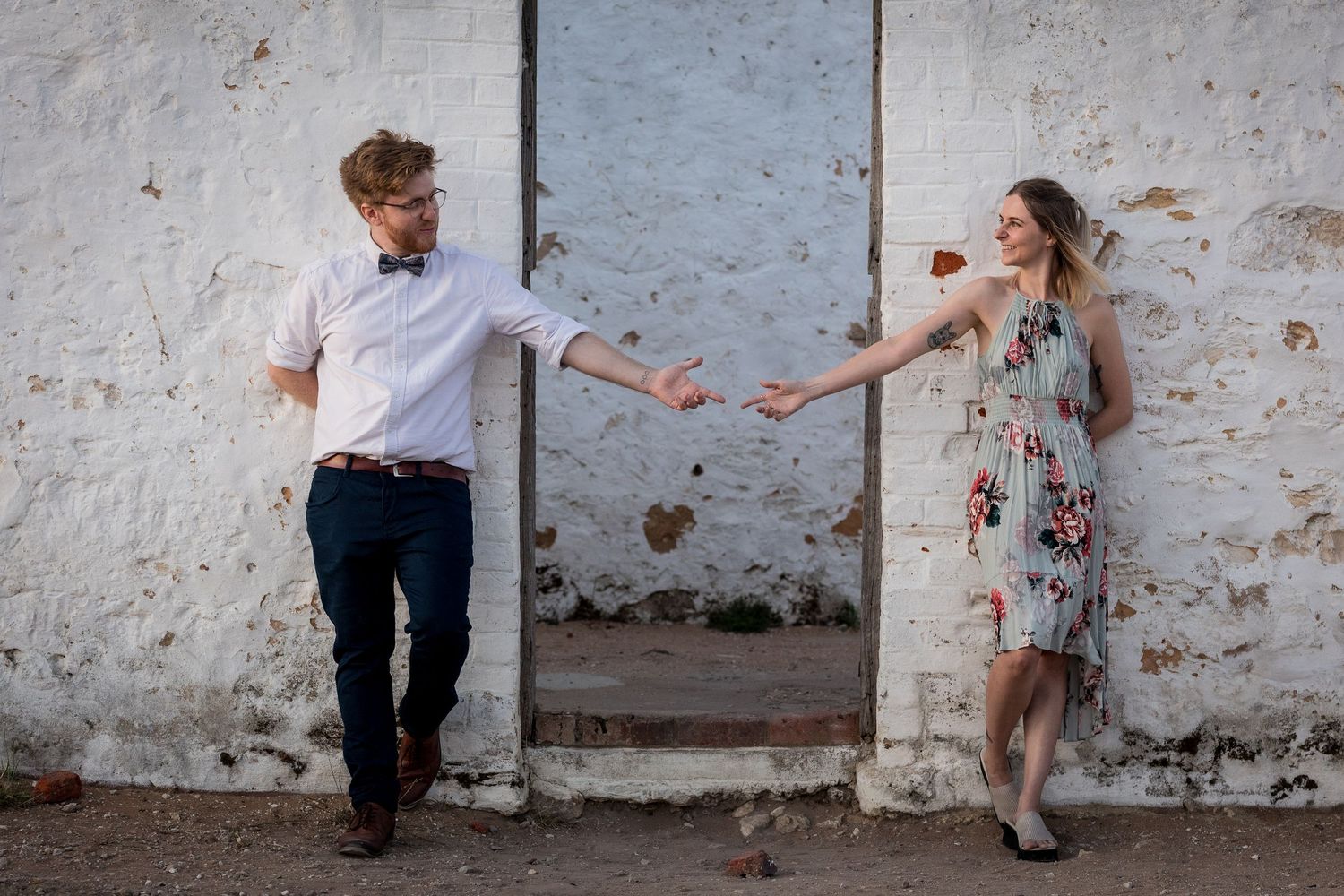 Couple dances playfully in front of white wall with doorway.