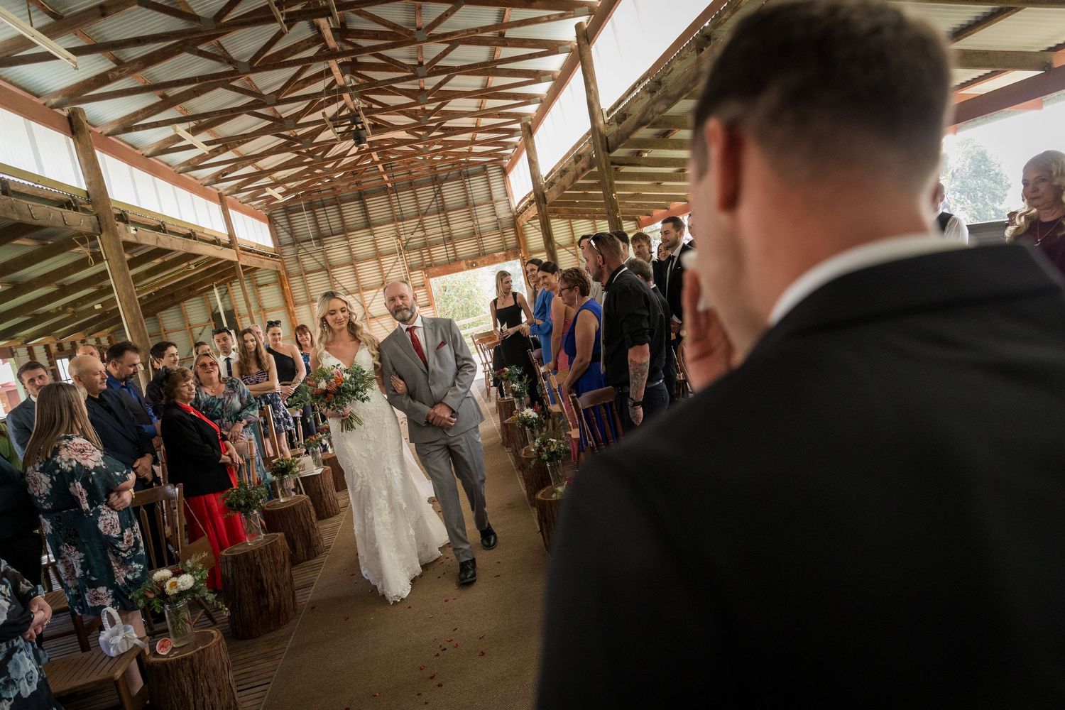 Wedding ceremony taking place in a rustic barn venue with exposed wooden beams and natural lighting.