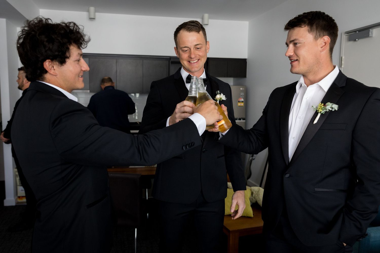 Groomsmen share drinks and laughs while getting ready for the wedding.