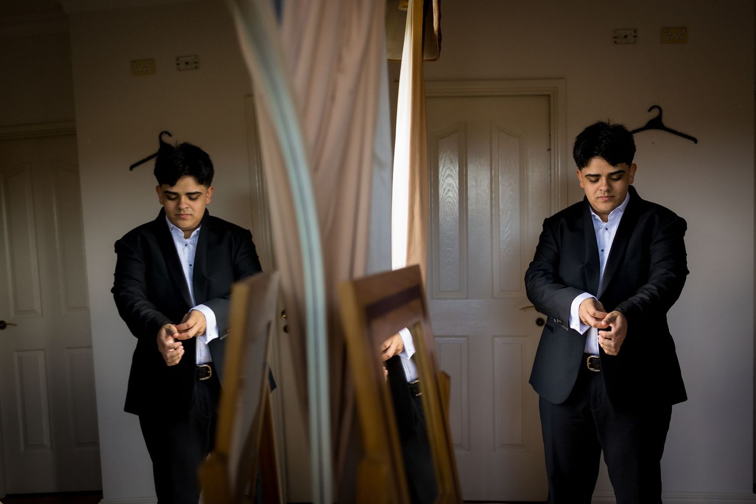 Person in formal attire adjusts clothing while looking in mirror.