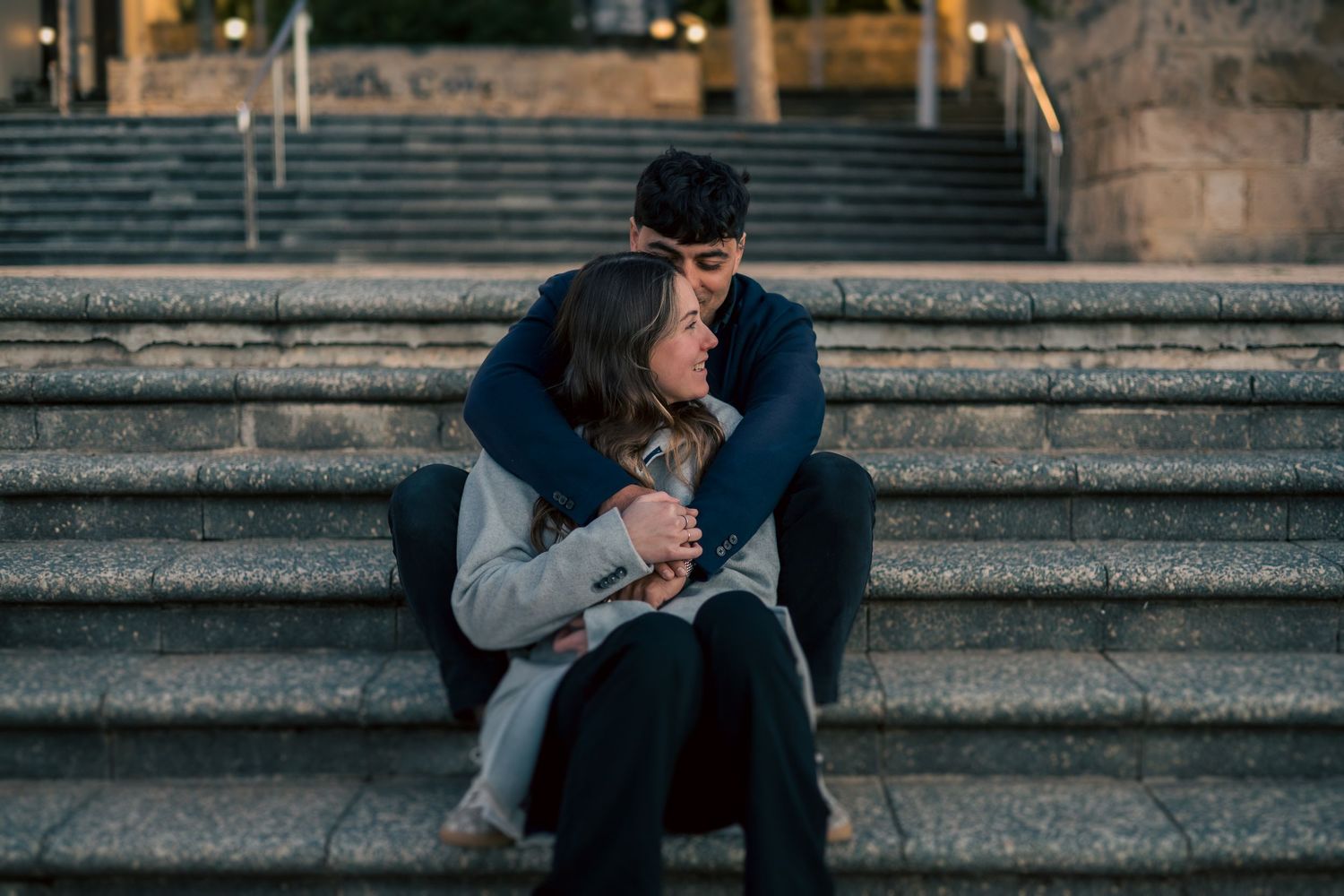 Two people share an intimate moment on stone steps during golden hour.