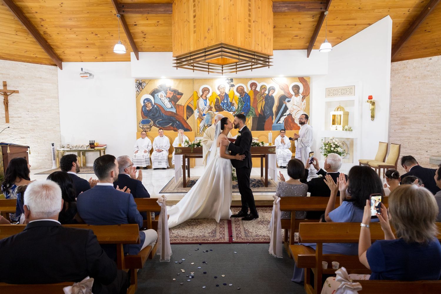 Bride and groom exchange vows at the altar of a small church with guests seated in wooden pews.