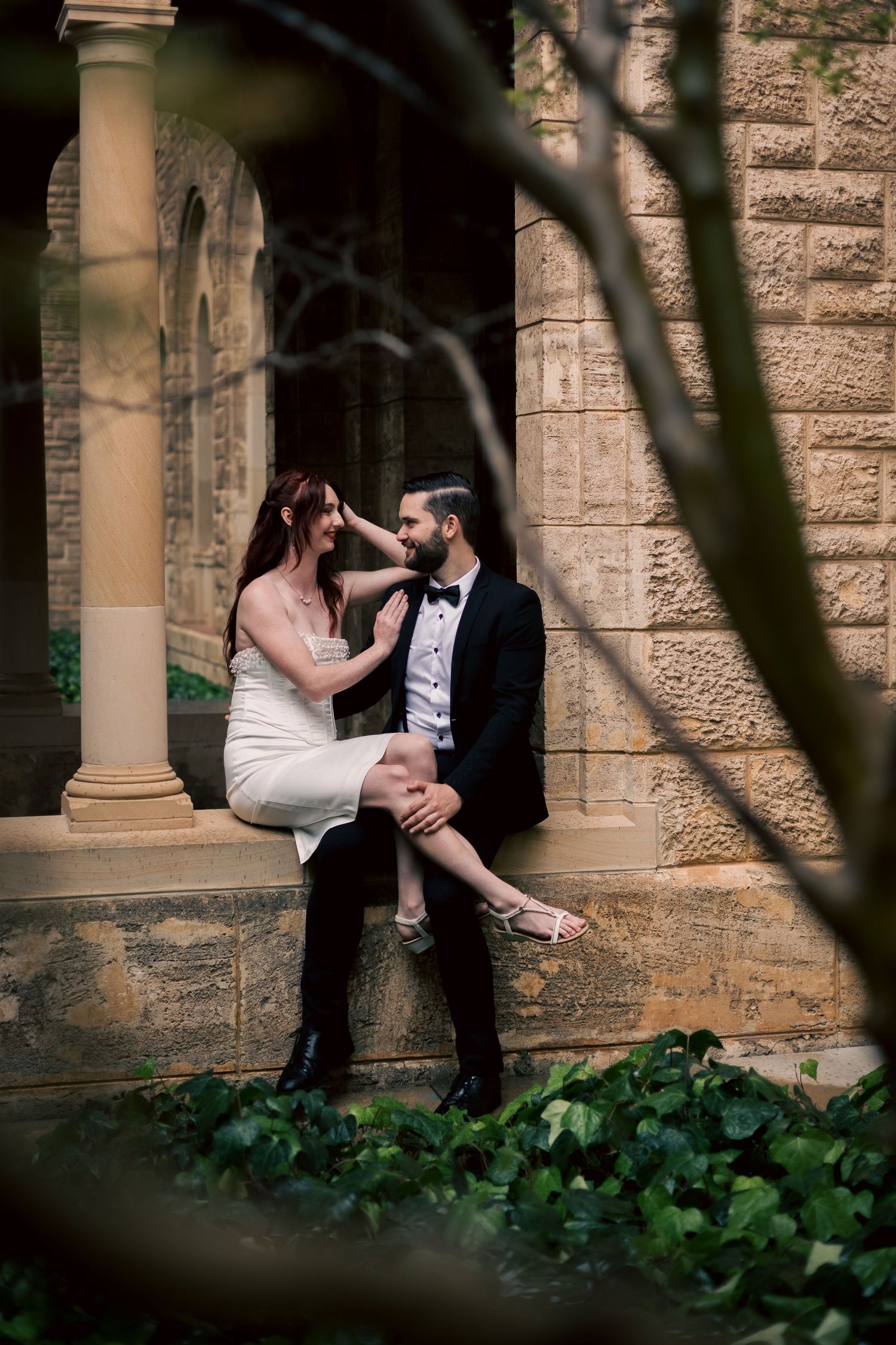 Romantic couple poses in formal wear against stone columns with ivy.