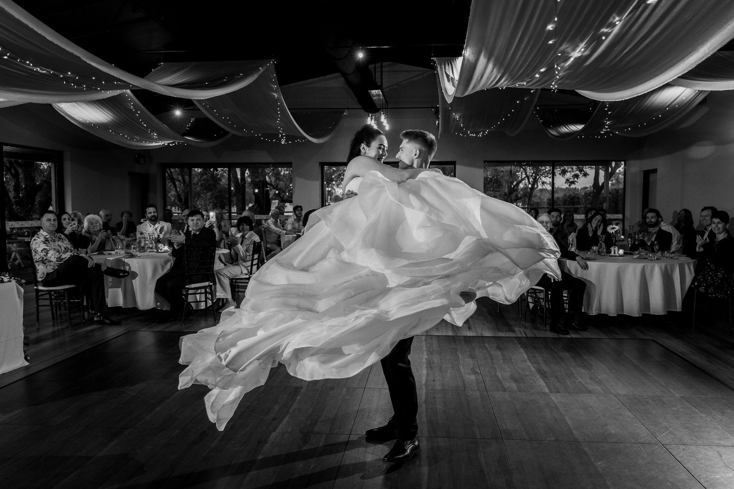 Wedding couple dances in dramatic lighting on indoor dance floor.