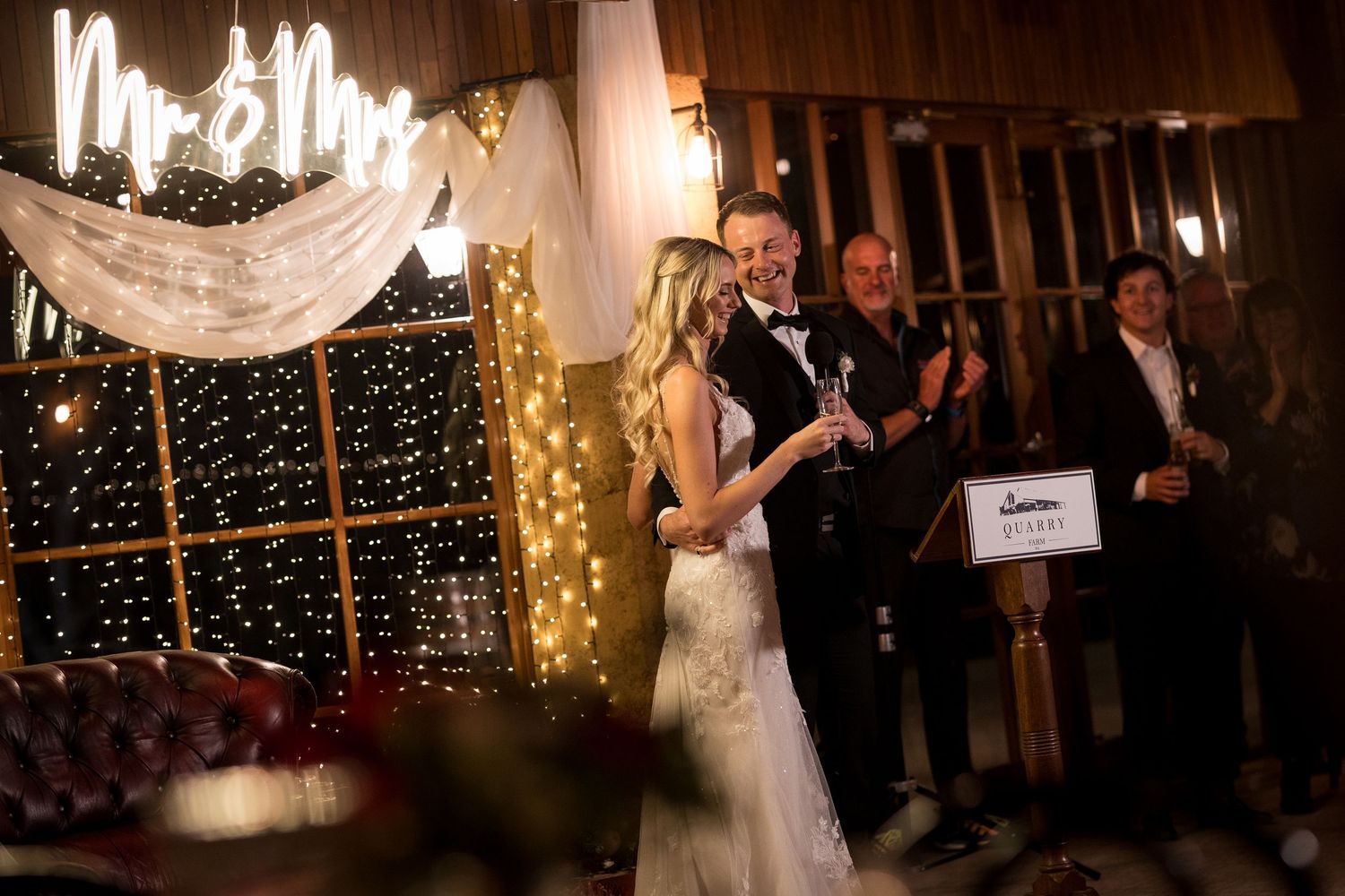 Wedding reception in barn venue decorated with twinkling lights and white draping.