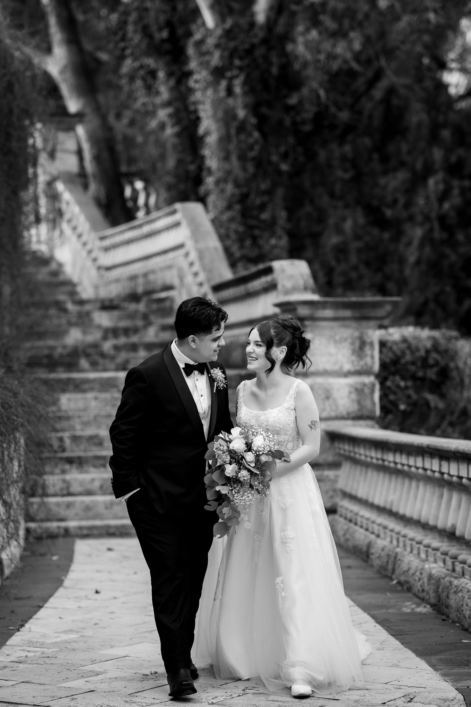 Wedding couple posing on stone steps surrounded by lush greenery.