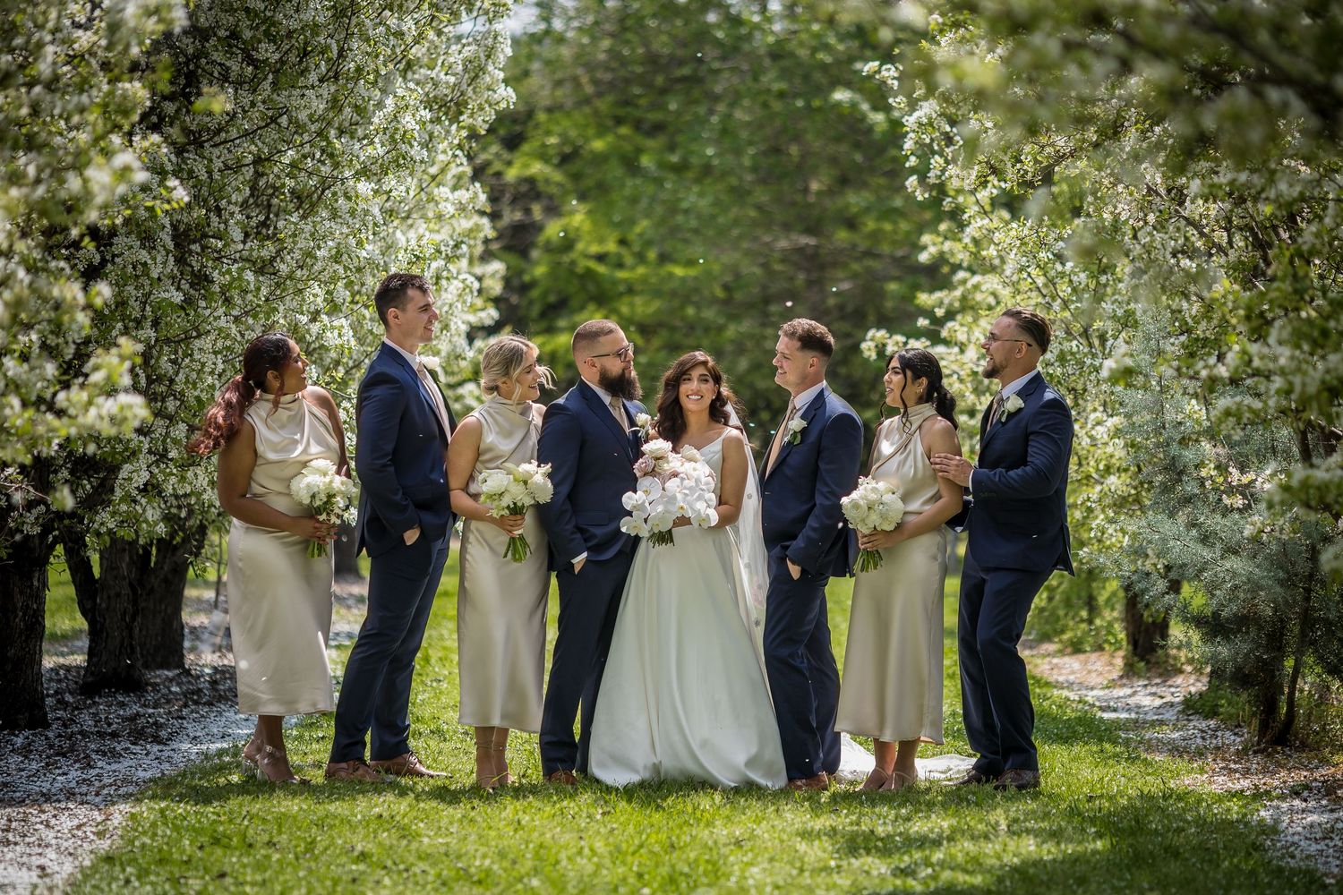 Wedding party poses among blooming white trees in a lush garden setting.