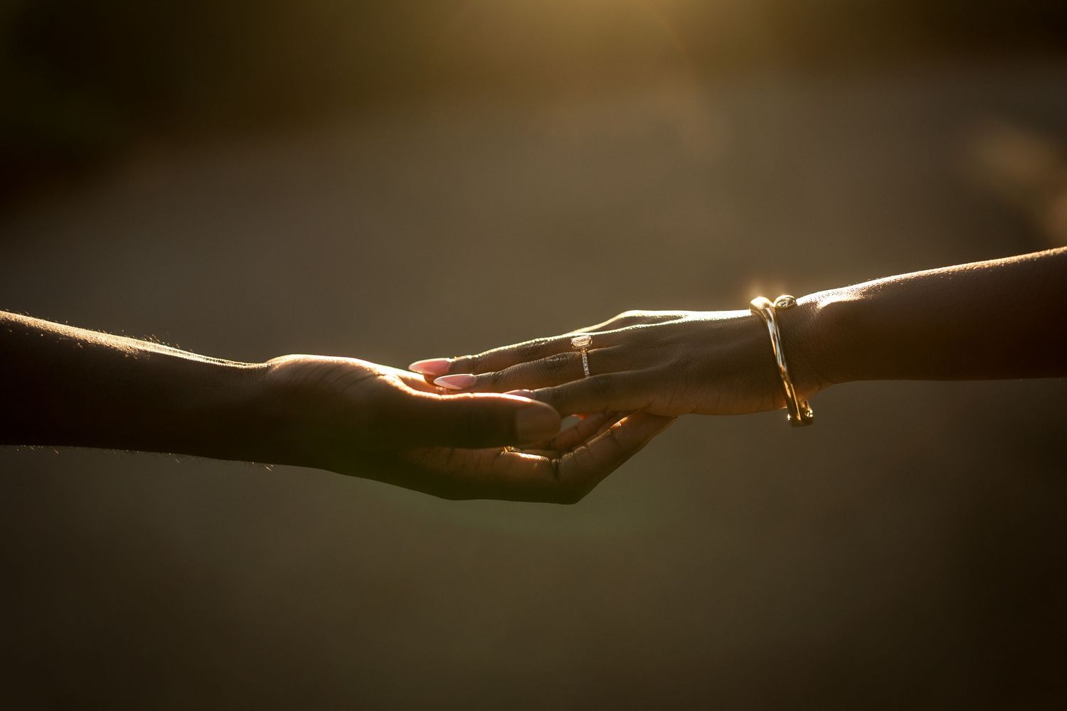 Two hands gently reaching toward each other in warm golden sunlight, one wearing a delicate bracelet, symbolizing connection and love.