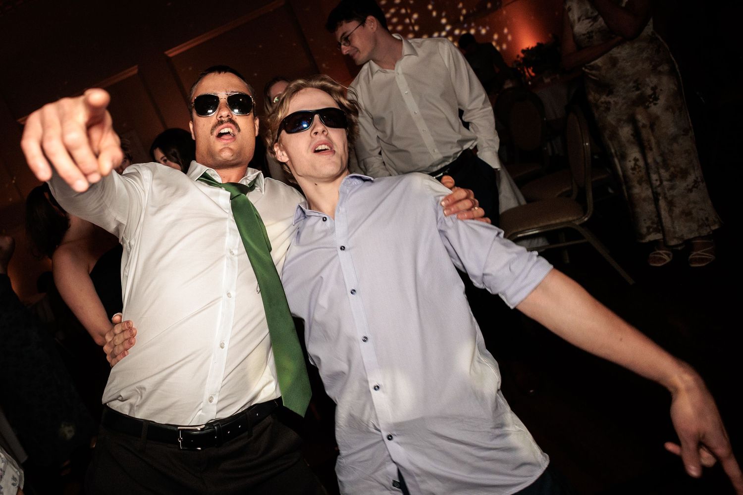 Two men wearing sunglasses dancing energetically at a party, one in a green tie and white shirt at Montgomery Hall