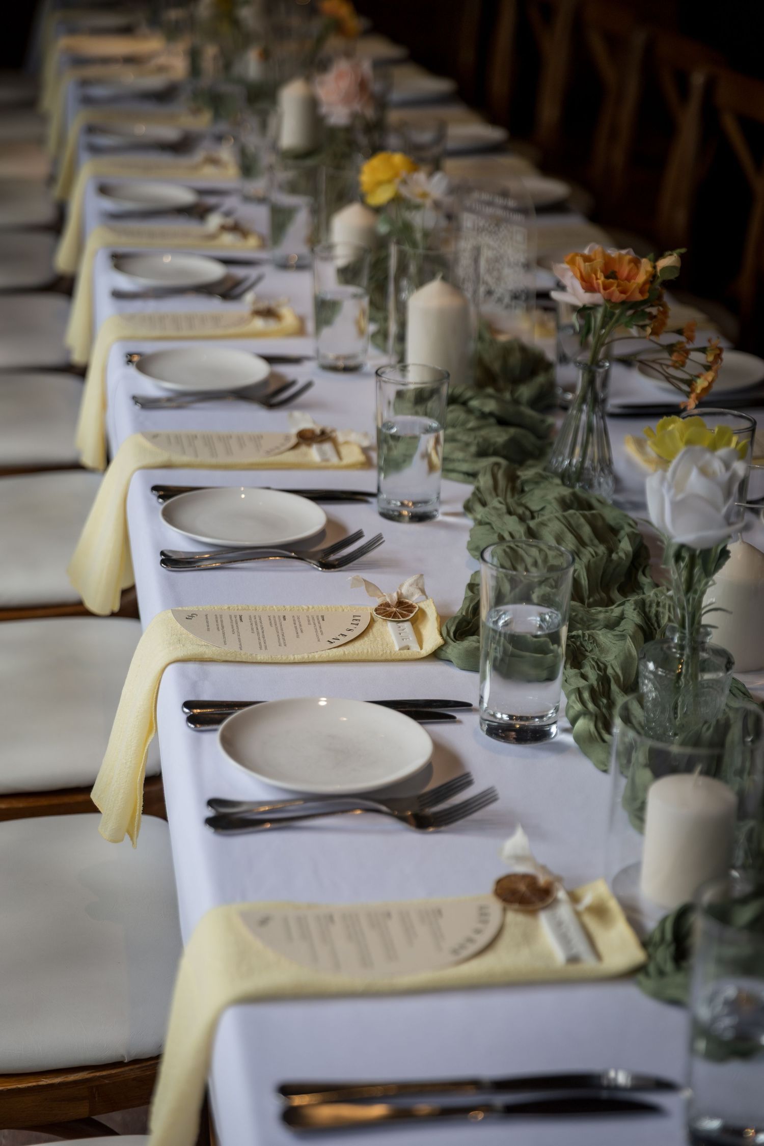 Elegant banquet table set with white plates, yellow napkins, floral centerpieces, and candles for a formal dinner event.