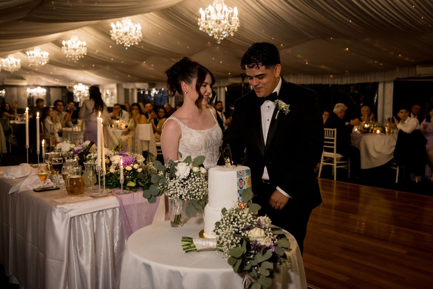 Couple shares an intimate moment at their wedding reception next to an elegantly decorated cake table.