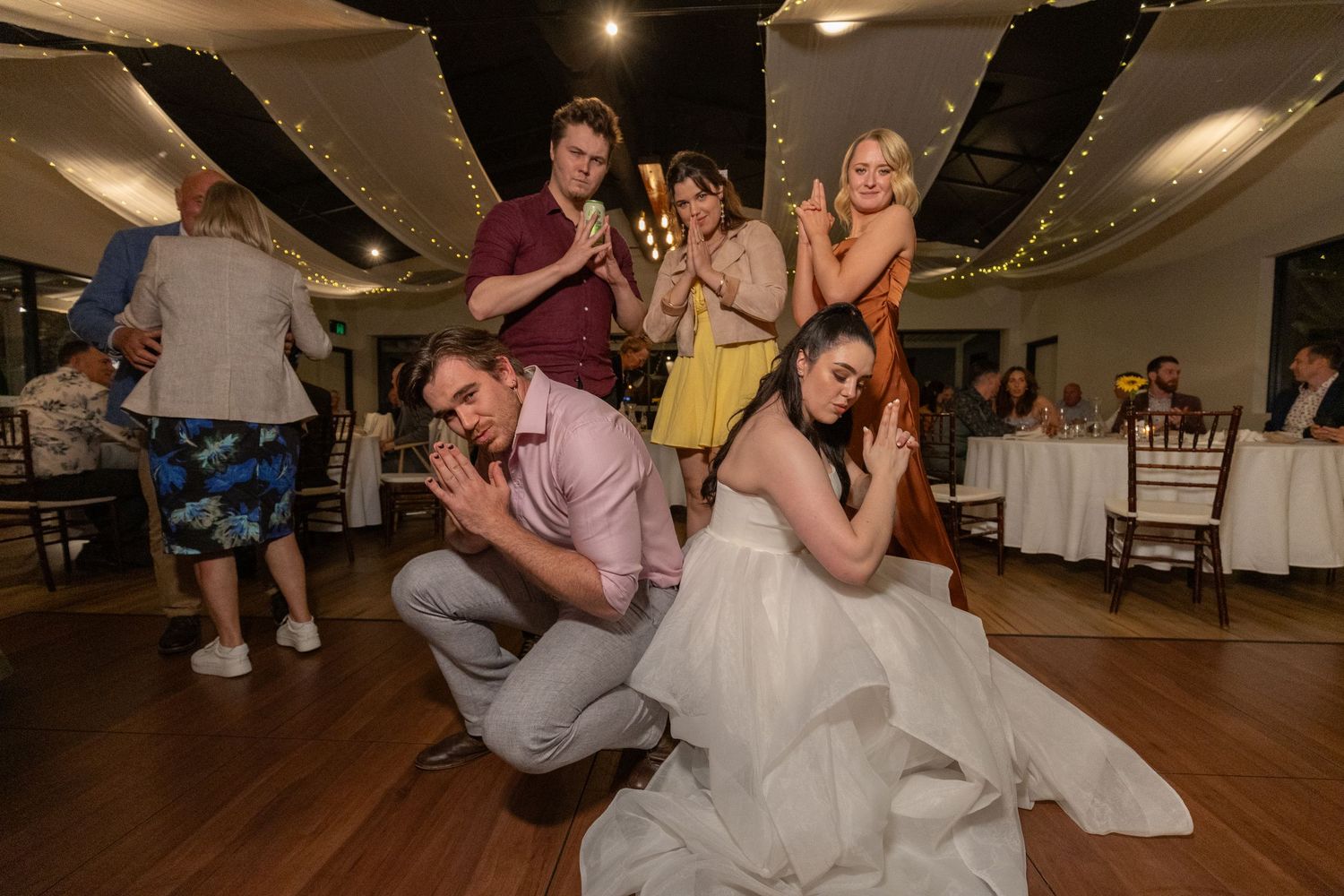 Fun group dance moment captured during wedding reception on wooden dance floor.