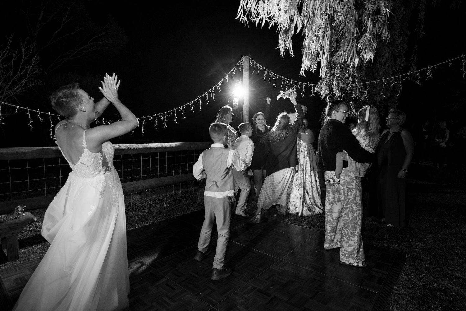 Silhouettes of wedding guests dancing under string lights create a romantic nighttime atmosphere.